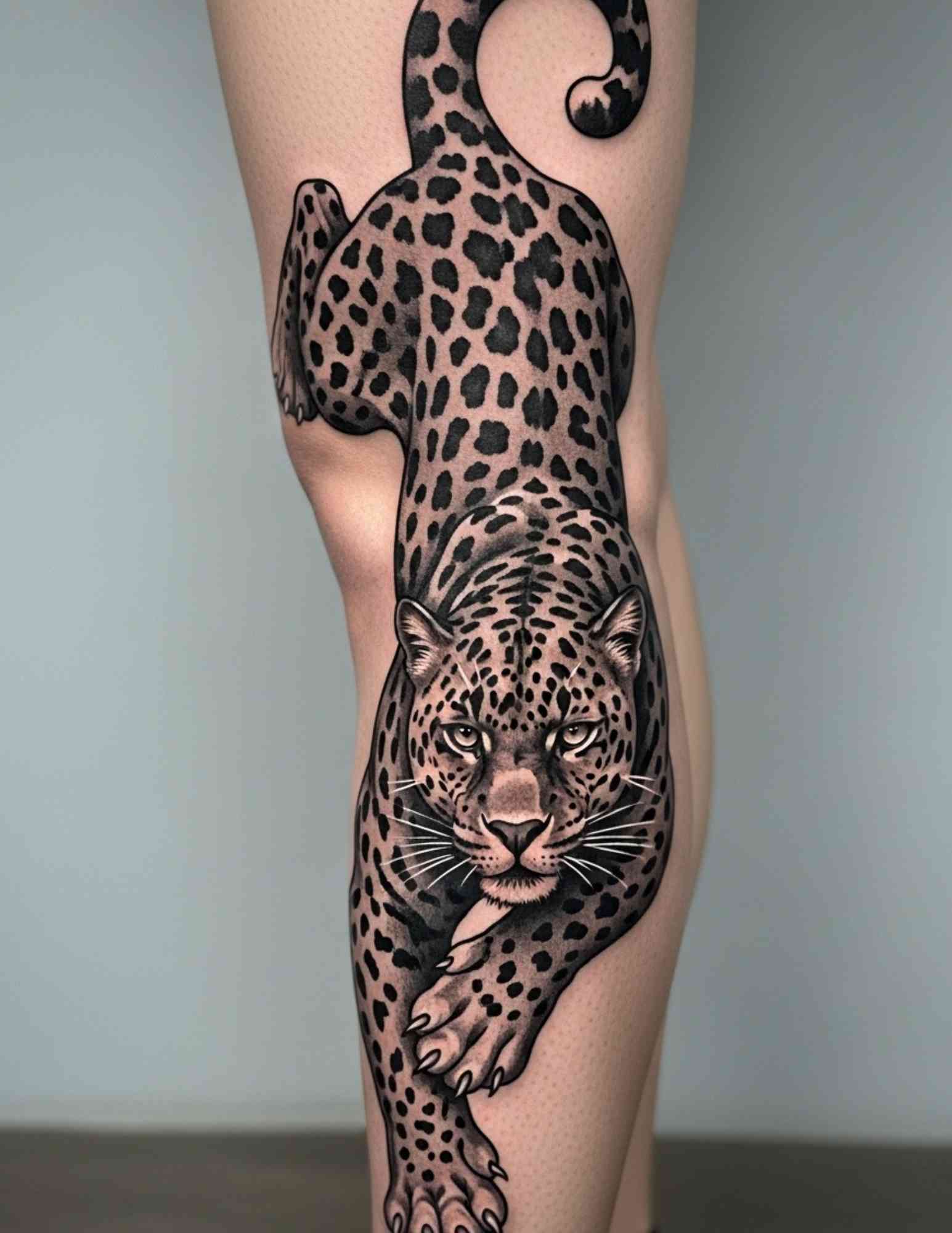 Panther tattoo climbing a leg with claws gripping and the head turned toward the viewer