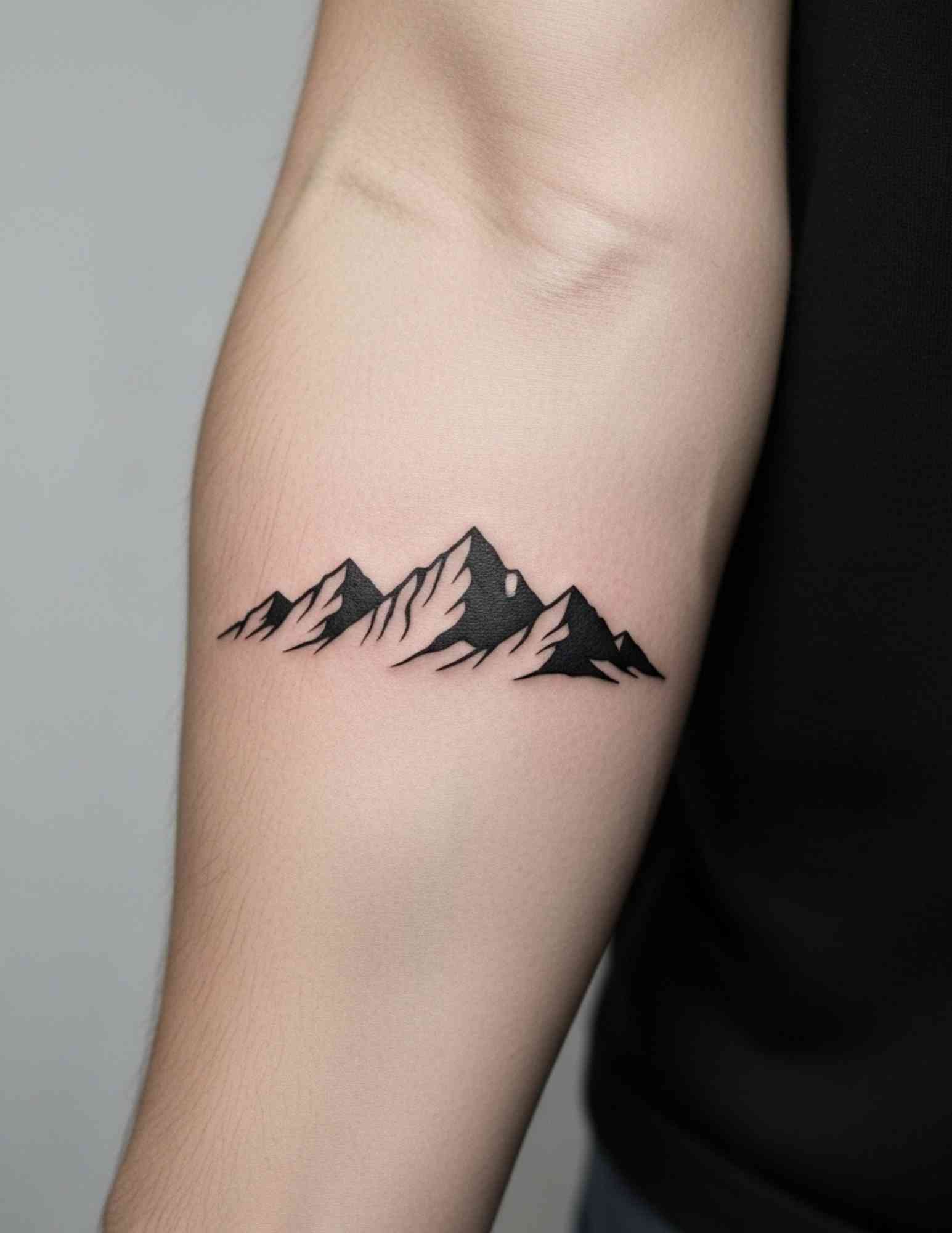 Blackwork mountain range silhouette tattoo on the forearm, a popular tattoo idea for teen boys