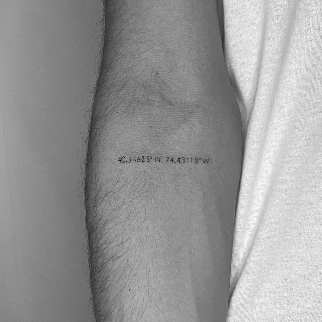 Coordinate tattoo marking a turning-point location, set in a bold technical typeface