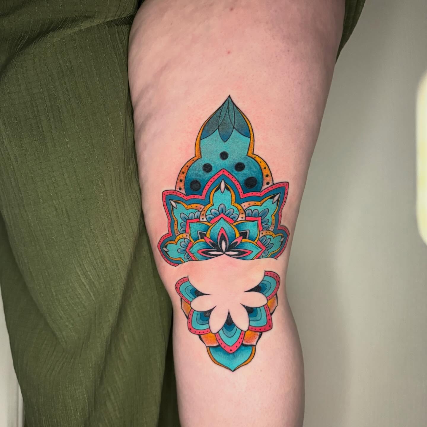Watercolor mandala tattoo in turquoise, orange and pink wrapping the back of a knee and thigh