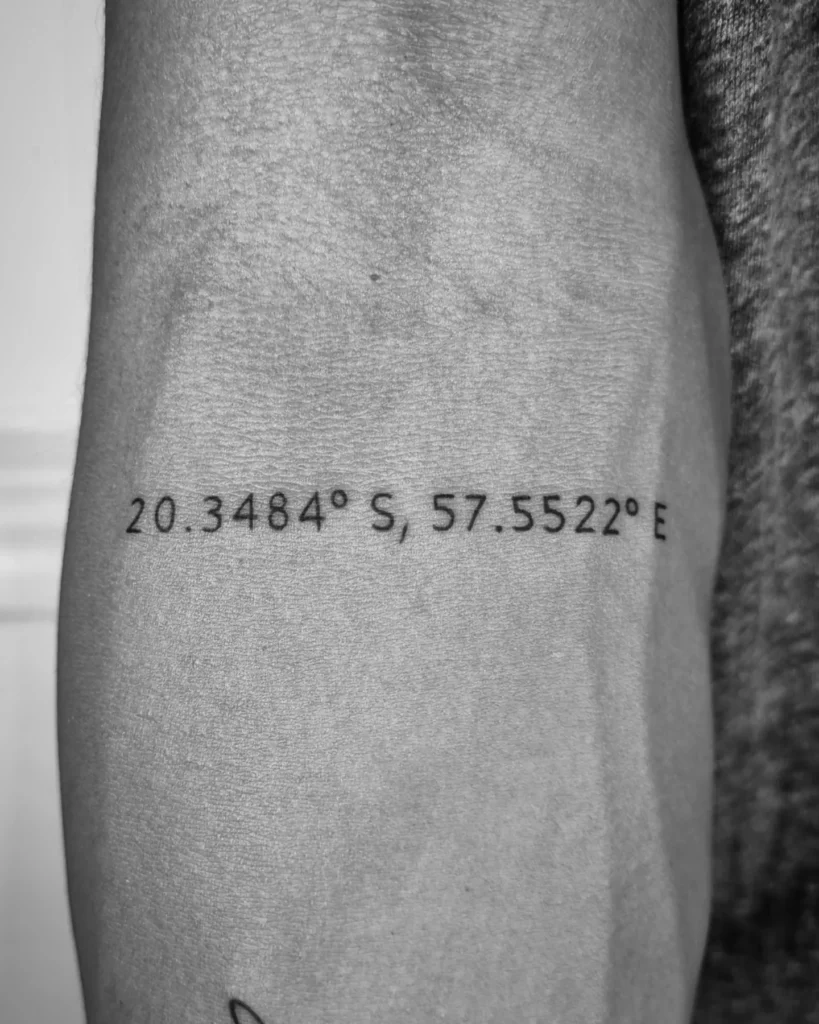 Coordinate tattoo of birthplace latitude and longitude in fine-line text on the forearm
