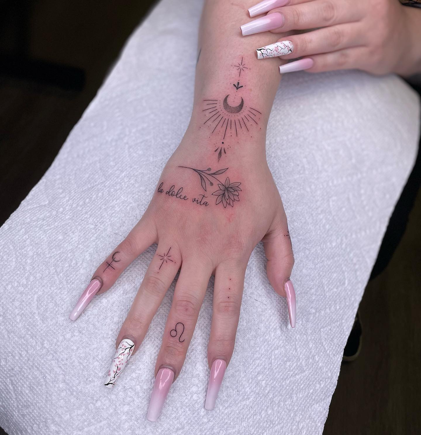 Fine-line hand and finger tattoos including a moon and small symbols, some of the most painful tattoo spots for their size.