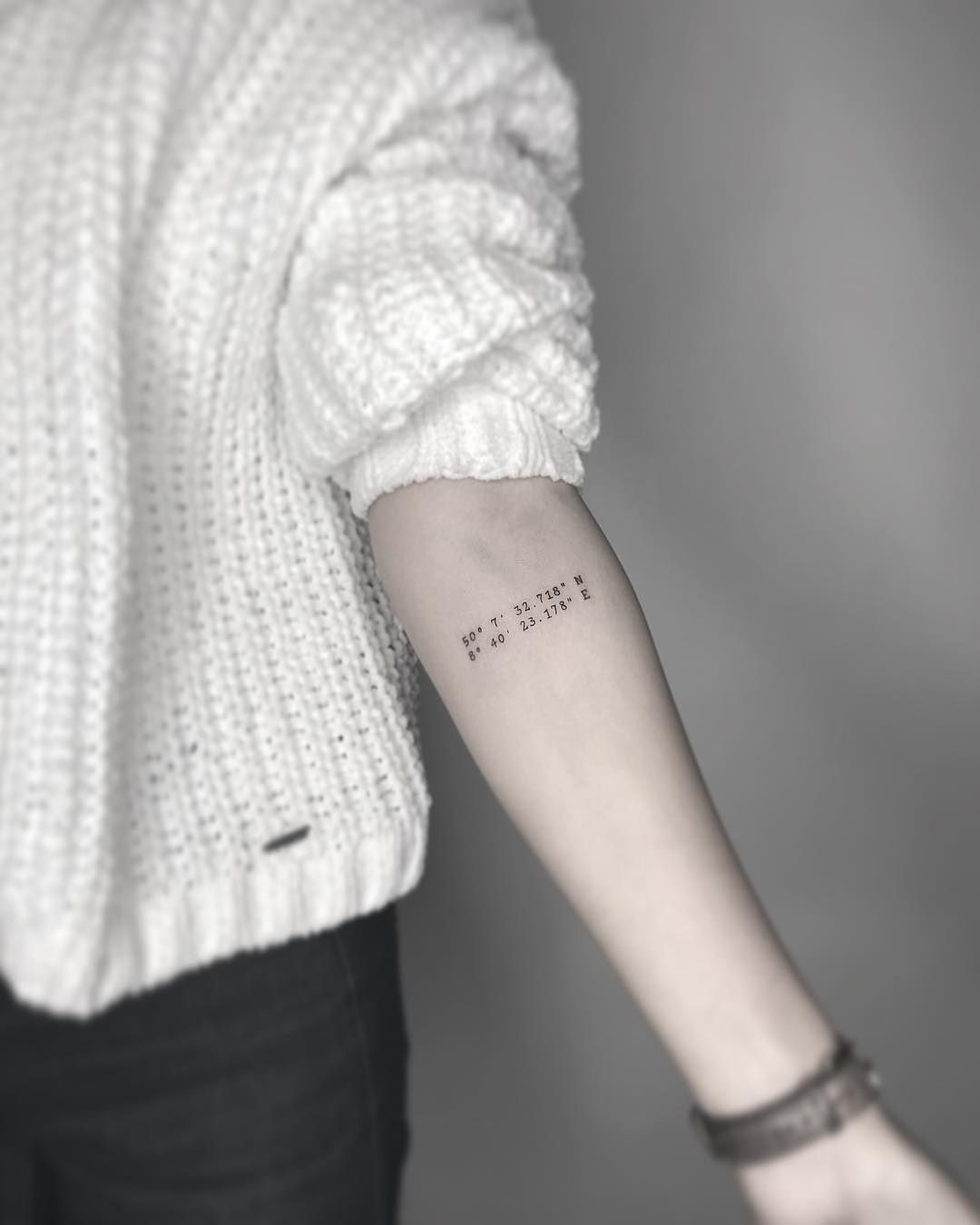 Coordinate tattoo marking a travel destination that prompted a life change, in fine-line script