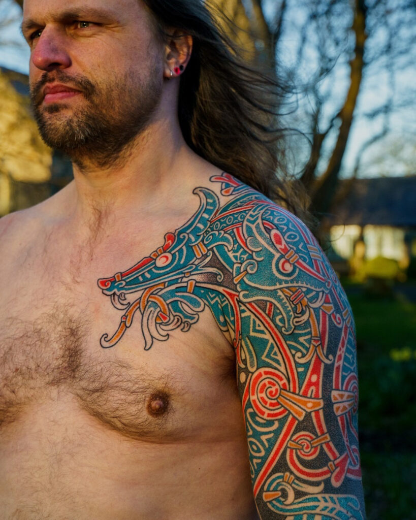 Norse mythology colorful sleeve tattoo with a warrior figure, runes and cold blue tones.