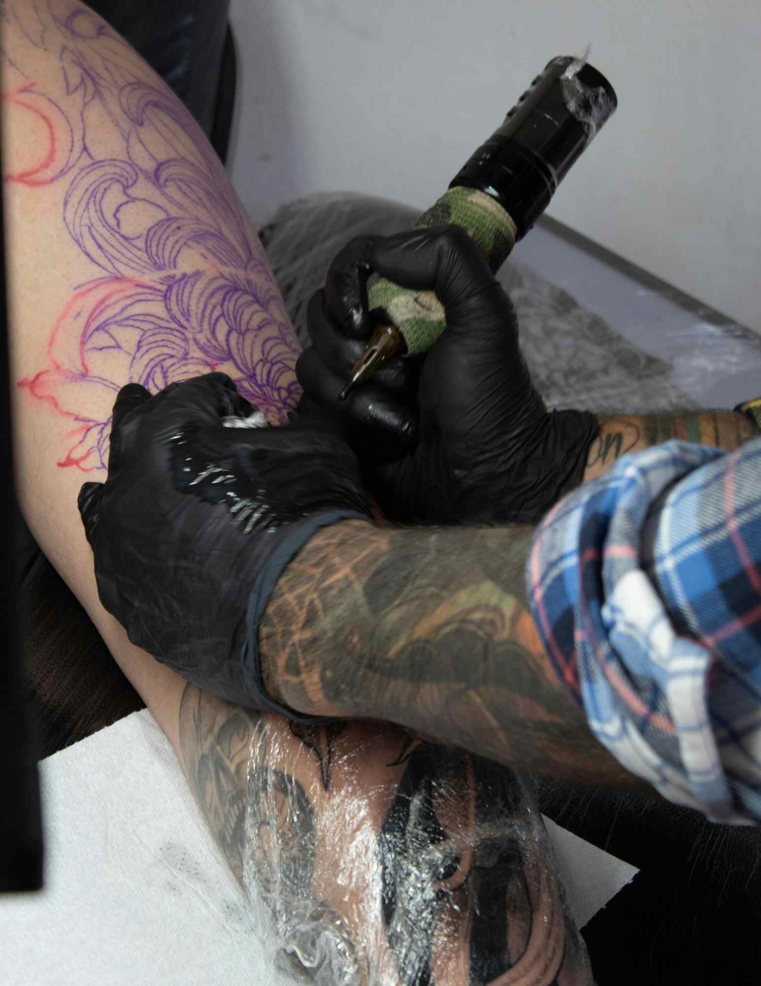Tattoo artist lining a leg tattoo design over a purple stencil