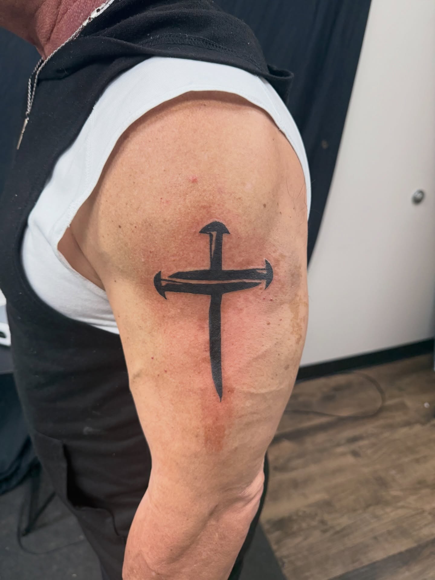 Cross spiritual tattoo in simple black linework on the upper arm