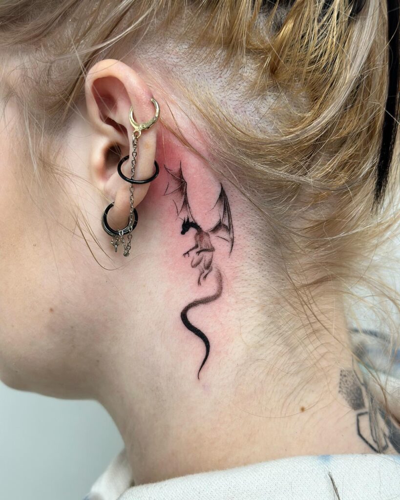 Small dragon tattoo for women placed behind the ear in delicate black linework