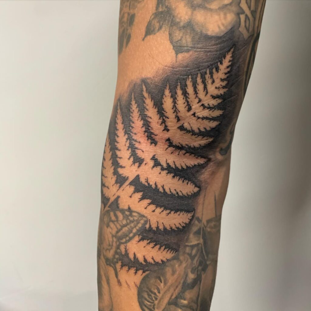 Negative space fern tattoo where the frond is left as bare skin inside a dark block