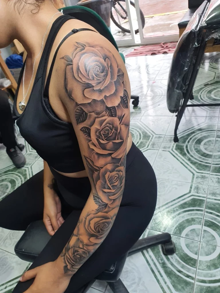 Dark floral rose sleeve tattoo rendered in heavy blacks and dramatic low-light shadow