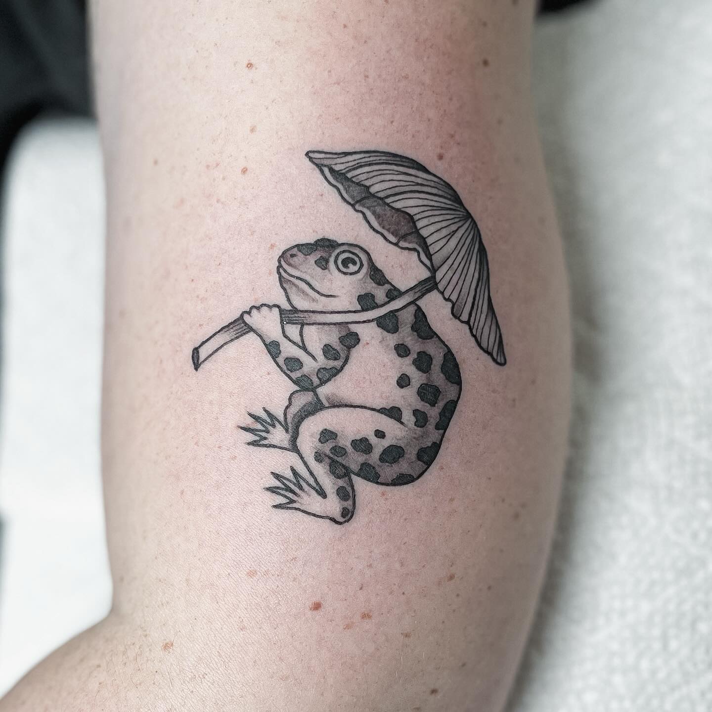 Frog with umbrella tattoo of a frog sheltering under a small parasol in the rain