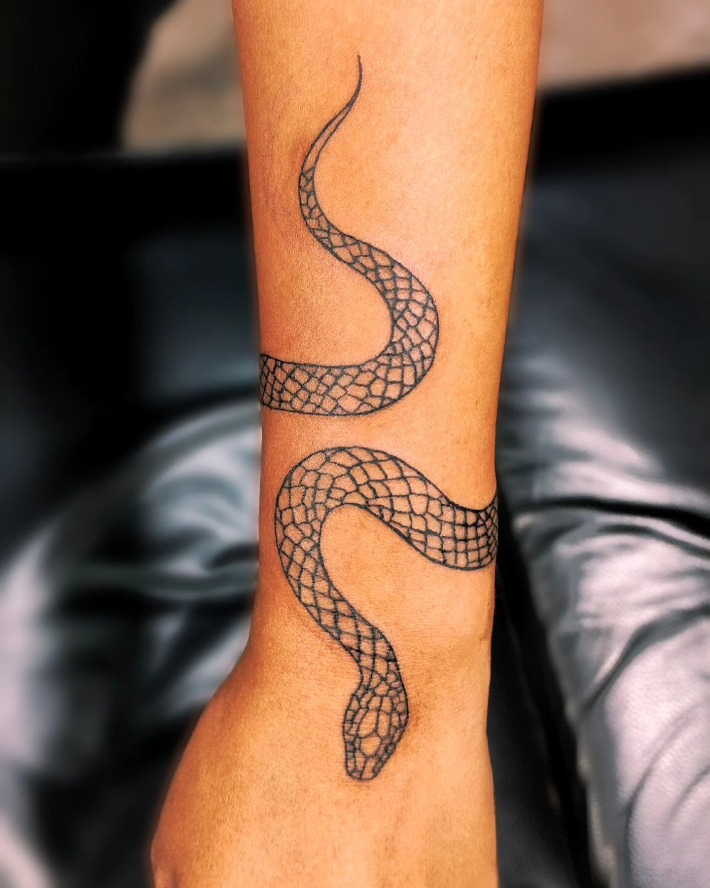 Snake wrist tattoo for men coiling around the wrist with the head on the outer side