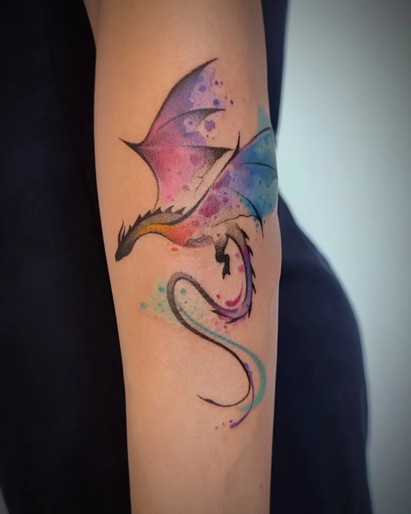 Watercolour dragon tattoo for women with soft blue and violet colour washes behind black linework