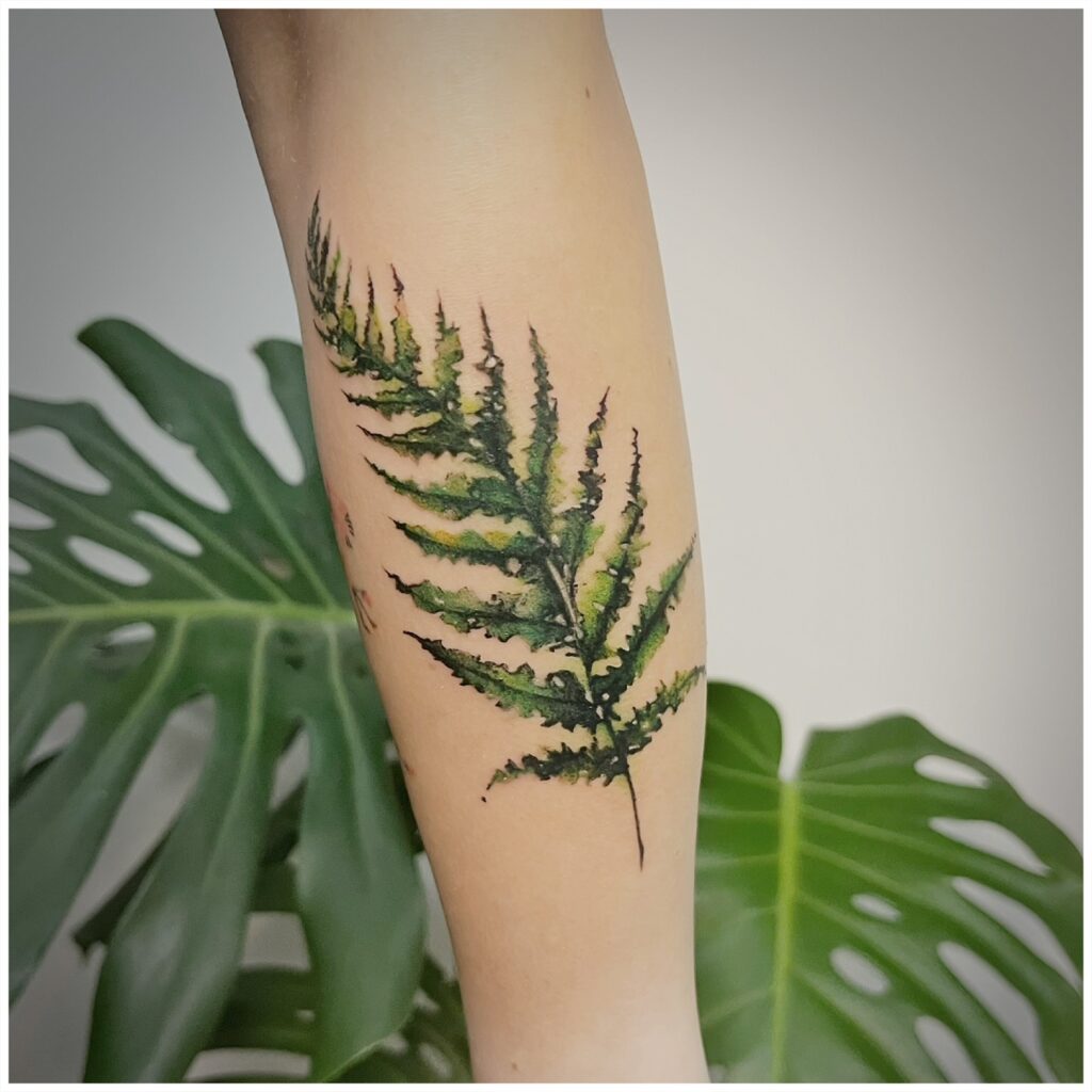Watercolour fern tattoo with soft green washes bleeding out past the linework