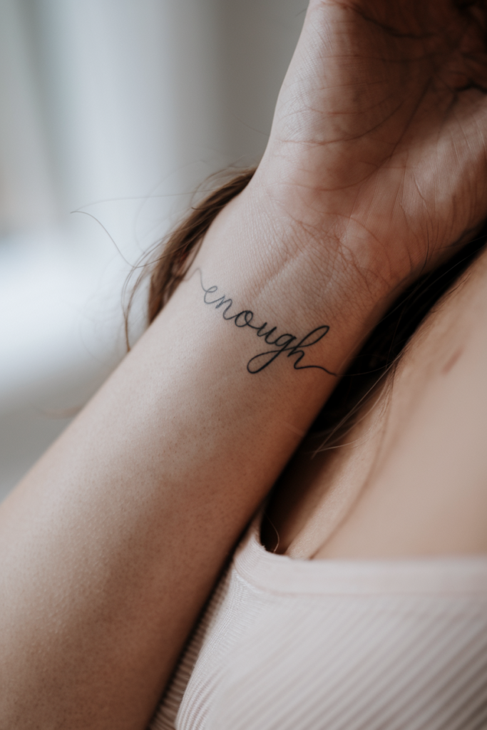 Fine cursive script reading enough tattooed along the inside of a forearm