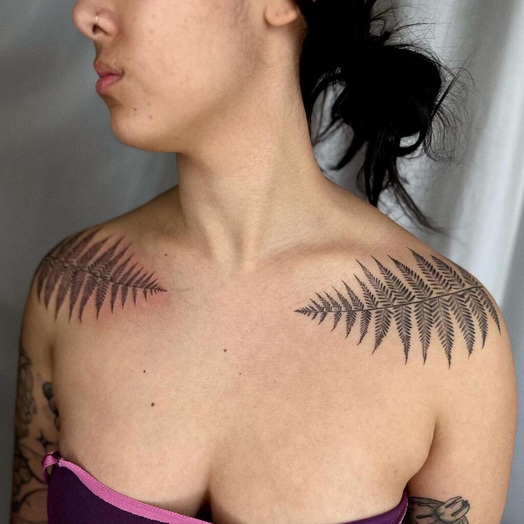 Fern shoulder tattoo with fronds arching from the shoulder blade onto the upper arm