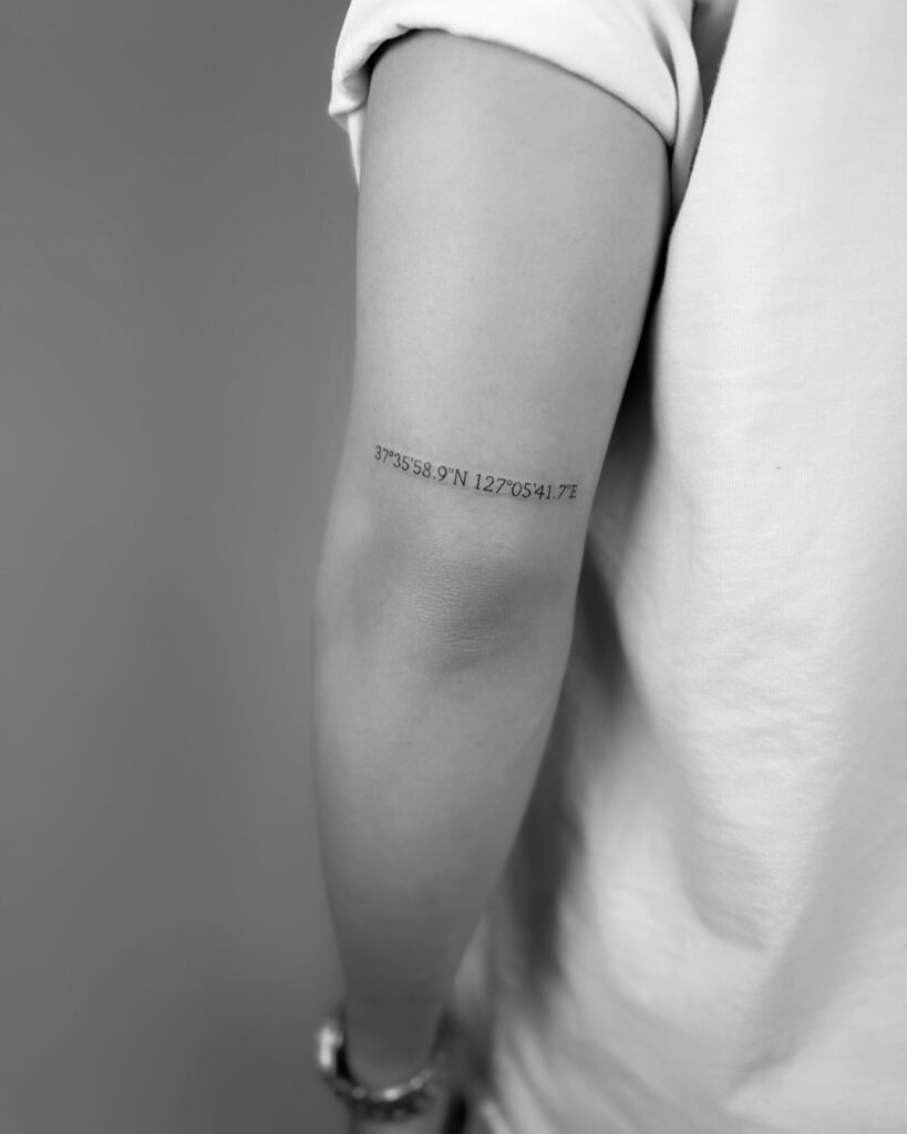 Hometown coordinate tattoo showing stacked latitude and longitude numerals in a clean sans-serif font