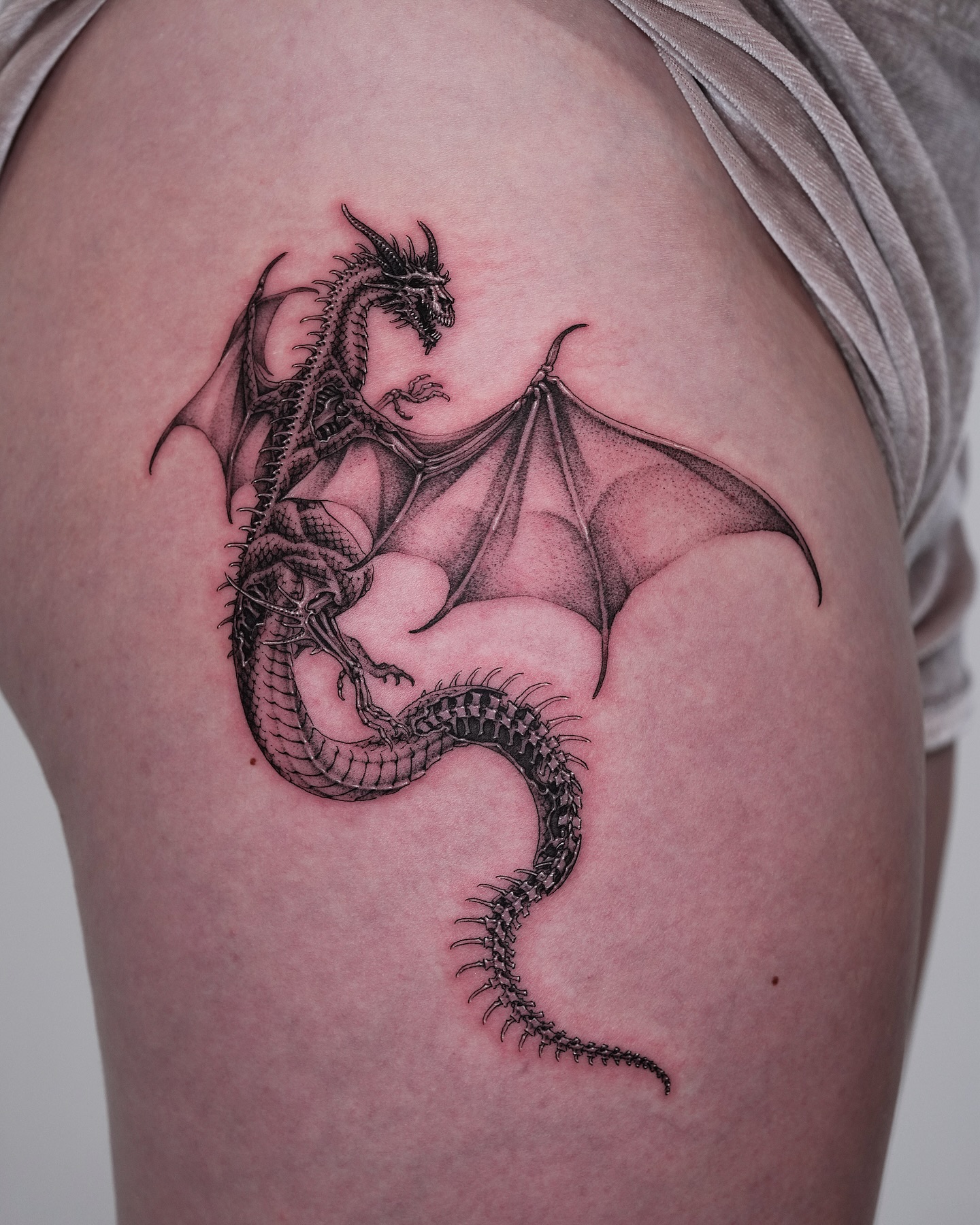 Dragon tattoo for women coiled protectively around a flower in fine black linework