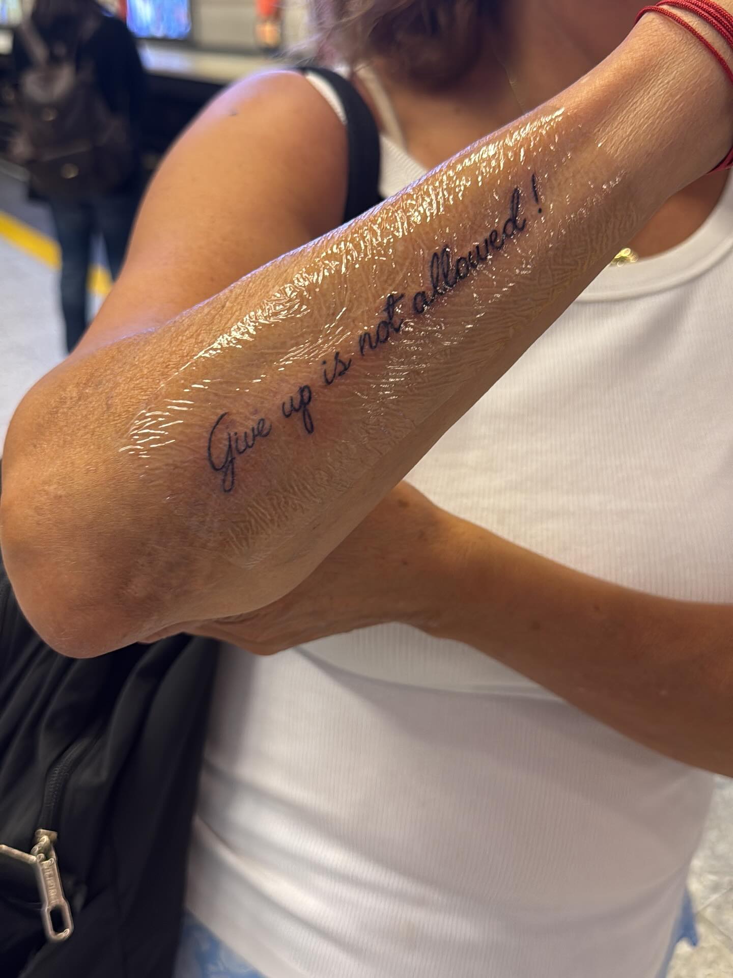 Clear Saniderm tattoo healing film sealed over a fresh script forearm tattoo reading Give up is not allowed