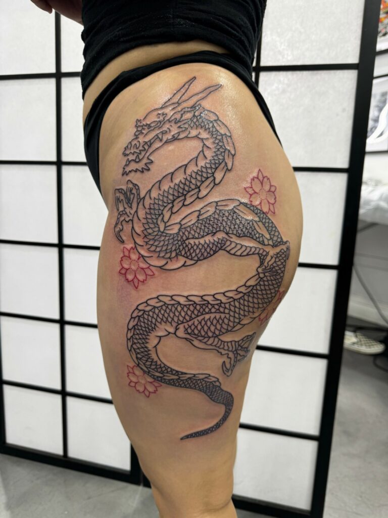 Serpentine dragon thigh tattoo for women coiling around the outer leg
