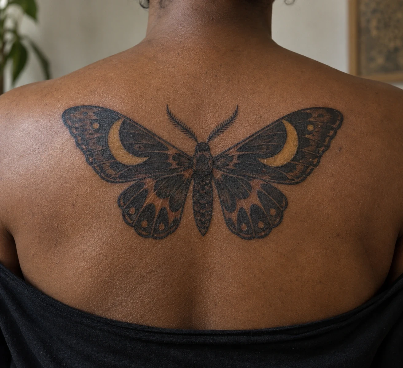 Black moth tattoo with ochre crescent patches across an upper back