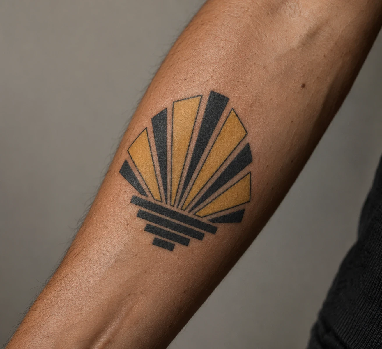 Art Deco fan tattoo with alternating black and ochre rays on a forearm