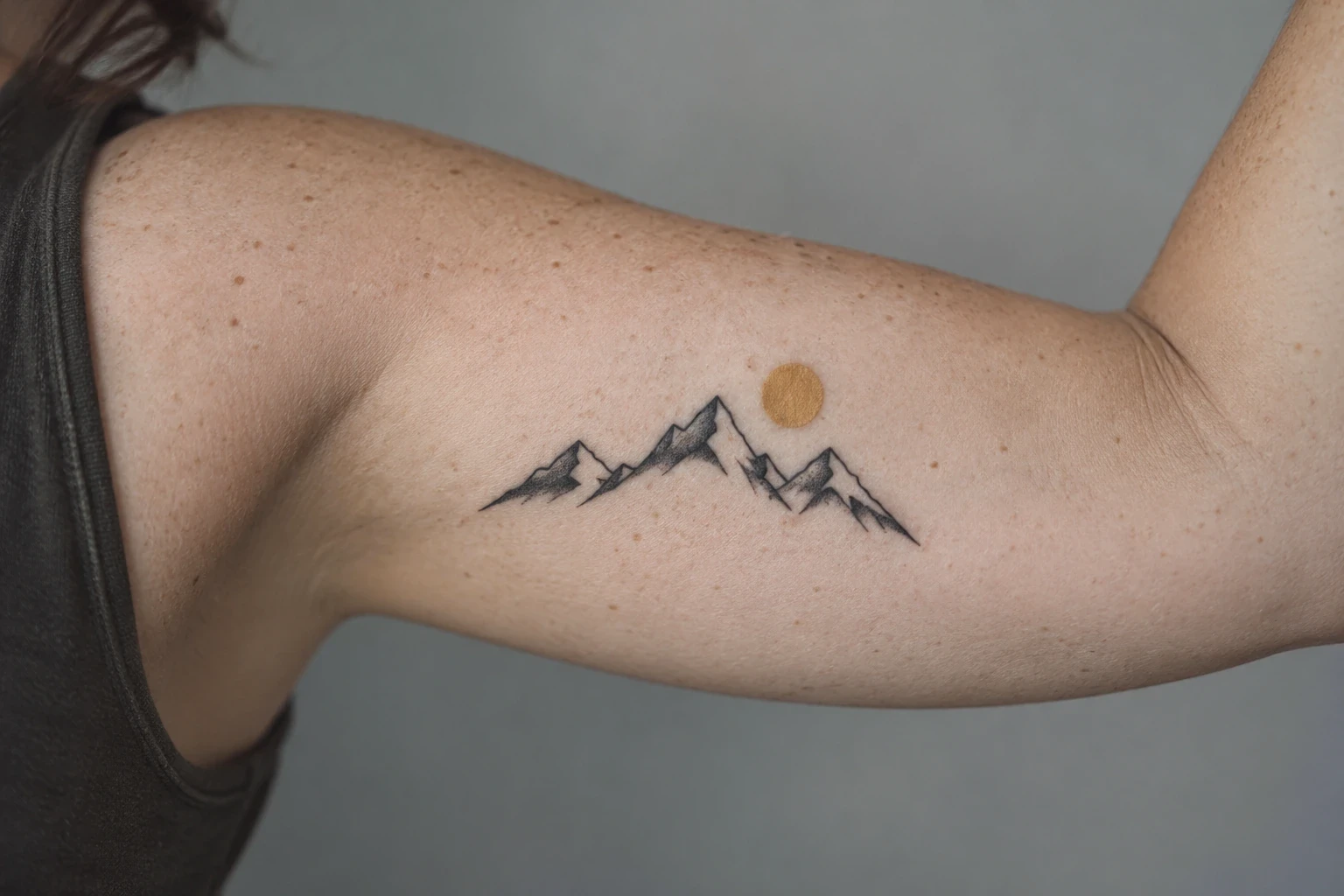 Three black mountain peaks and an ochre sun disk on an inner upper arm