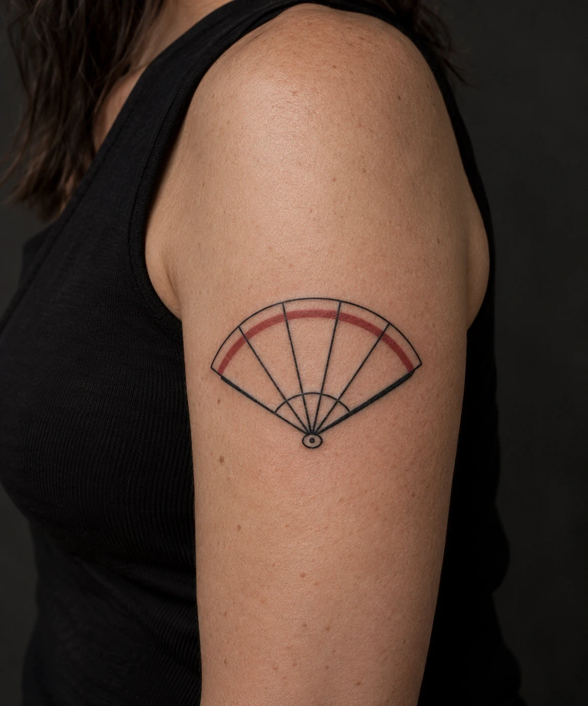 Open folding-fan tattoo with a red outer arc on an upper arm