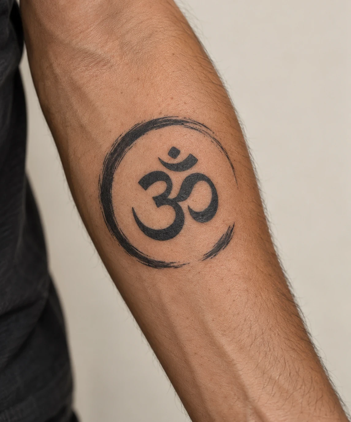 Black Om symbol inside an open brushstroke circle on a forearm