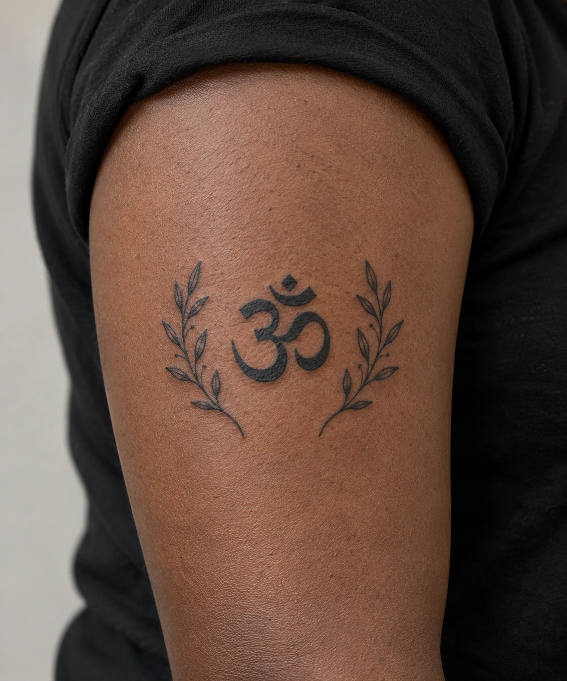 Black Om symbol between two fine botanical sprigs on an upper arm