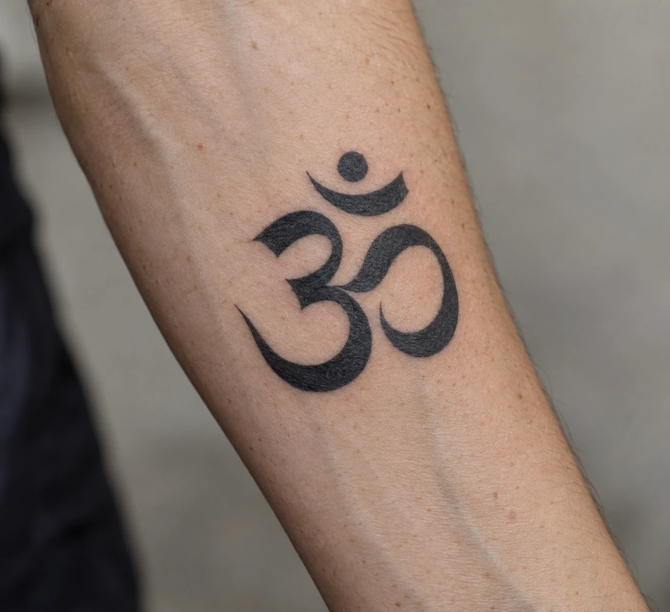 Black calligraphic Om tattoo with tapered strokes on a forearm