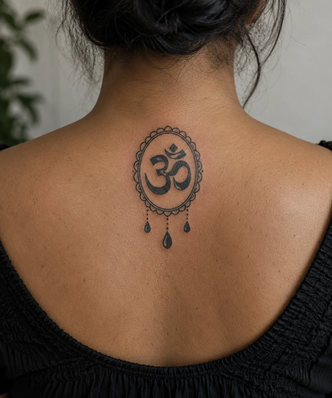 Black Om tattoo inside a scalloped oval with three teardrop ornaments on an upper back