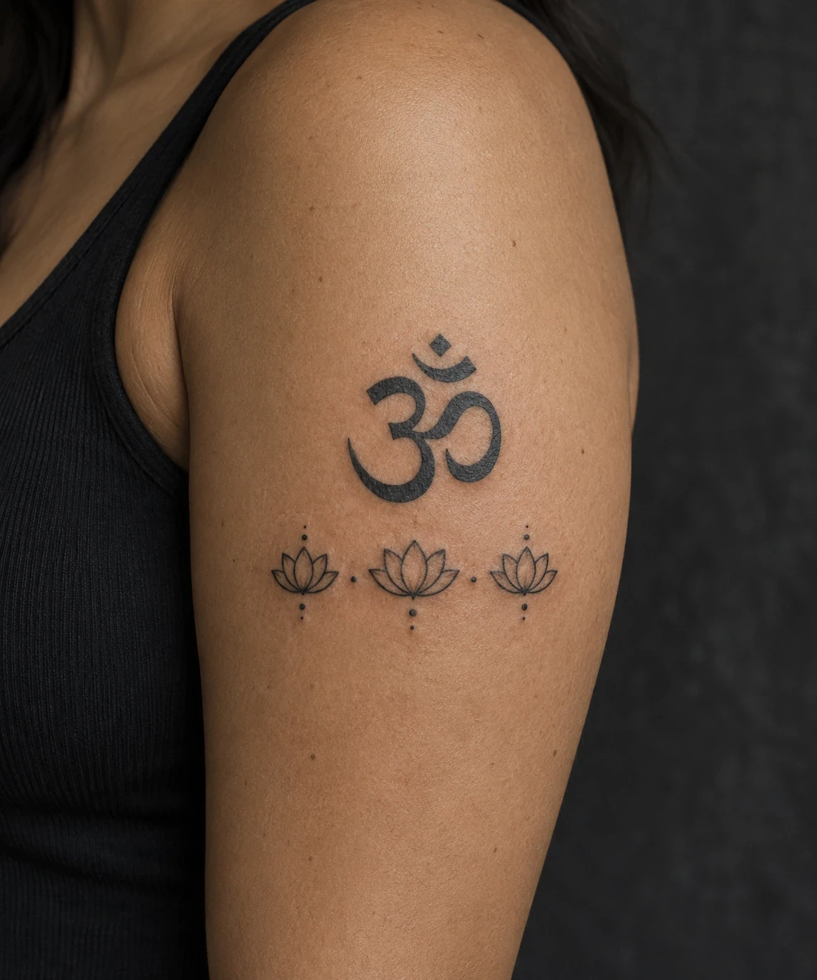 Black Om symbol above three small outlined lotus flowers on an upper arm
