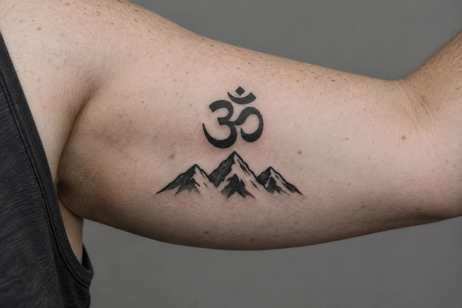 Black Om tattoo above three mountain peaks on an inner upper arm