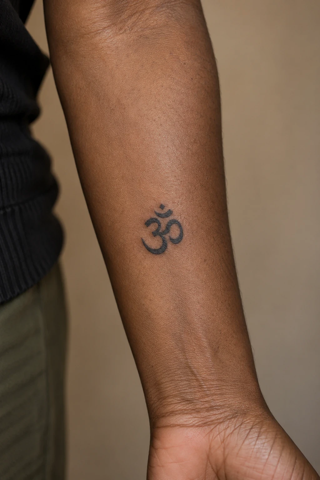 Small black Om tattoo with separate crescent and dot on an inner forearm